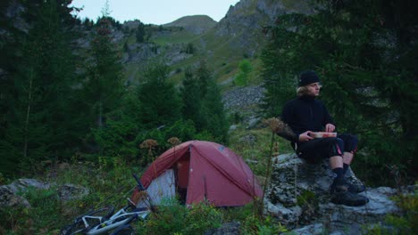 A-mountain-biker-is-eating-by-his-tent-in-an-alpine-valley