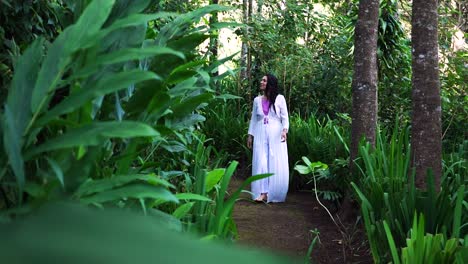 A-woman-walking-into-the-forest,-looking-at-the-lush-vegetation-and-the-green-leaves-in-awe