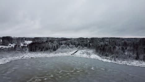 Aerial-rotating-drone-view-of-a-frozen-lake-and-a-dark-forest-in-cold-winter