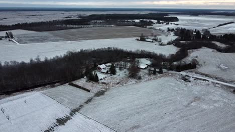 Luftdrohnenansicht-Von-Landhäusern-Und-Ackerland,-Die-Im-Dunklen-Winter-Mit-Einer-Schneeschicht-Bedeckt-Sind