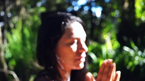 A-woman-practising-yoga-meditation,-in-a-beautiful-nature-environment,-moving-her-hands-from-her-forehead-to-her-chest