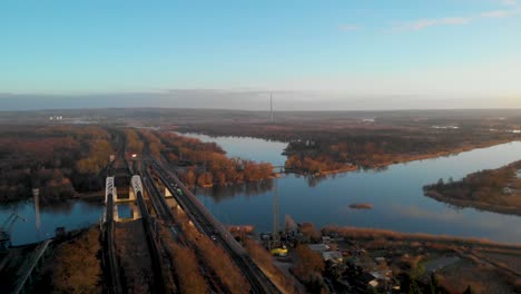 Vista-De-Pájaro-Del-Puente-Ferroviario-Y-La-Carretera-Con-Vehículos-Que-Viajan-Sobre-El-Río-En-Polonia