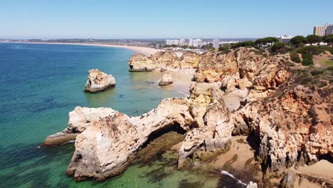 Aerial-Drone-View-of-Praia-dos-Tres-Irmaos-Beach-in-Algarve,-South-Portugal---Beautiful-Coastline-with-Rocky-Cliffs,-Tourists,-Hotels-and-Clear-Blue-Sea