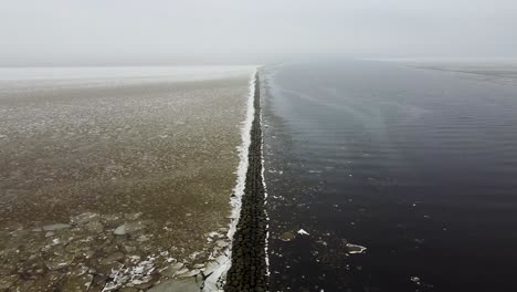 Rising-aerial-drone-view-of-a-long-stone-sea-mole-breakwater-in-winter