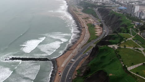 Reveal-shot-of-Miraflores-city-near-the-beach-with-a-coastal-road-in-Peru-aerial