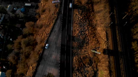 Bird's-Eye-View-Of-Vehicles-Driving-At-Asphalt-Road-Adjacent-To-Railroad-At-Sunset