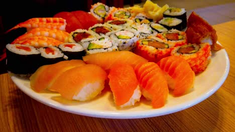 Sushi-Rollen-Maki-Sortierte-Runde-Weiße-Platte,-Die-Sich-Auf-Einem-Holztisch-Im-Restaurant-Dreht,-Wo-Schatten-Von-Menschen,-Die-Im-Hintergrund-Vorbeigehen