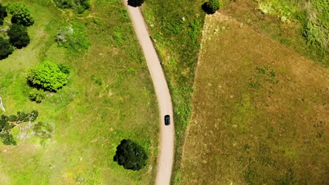 Aerial-Birds-Eye-View-following-Black-Car-Traveling-along-Small-Country-Road