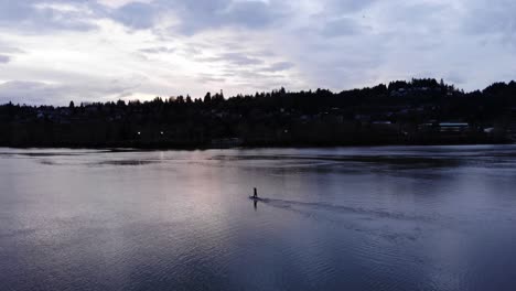 Wide-shot-Slow-Pan-left-Silhouette-of-a-Paddle-boarder-traveling-along-Willamette-River,-Portland-Oregon