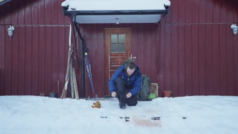 Man-Tying-Boots-In-Front-Of-His-Cabin-At-Winter