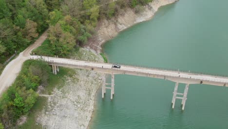 Aerial-drone-view-of-the-car-crossing-from-a-small-bridge-over-Turano-lake,-Lazio,-ITALY