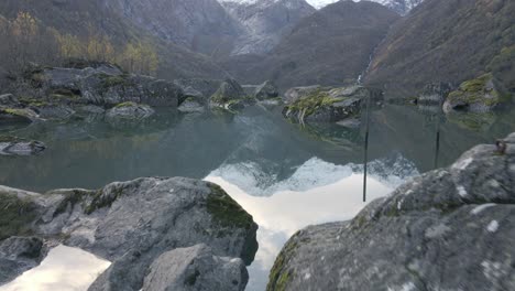 Rocks-in-majestic-mountain-lake-with-snowy-peek-reflection-in-water,-dolly-forward-tilt-up-shot