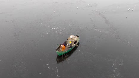 Top-view-of-two-nordic-fishermen-in-a-green-boat-fishing-on-a-frozen-water-in-a-cloudy-winter-day