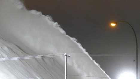 Snow-spraying-from-Snowblower-to-massive-white-snow-pile,-Cleaning-road-at-night,-Detail-view