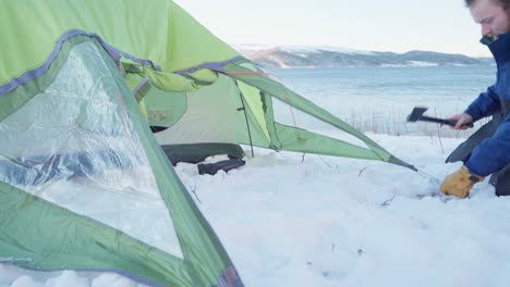 Man-Building-A-Waterproof-Tent-Putting-Stake-On-Snowy-Ground