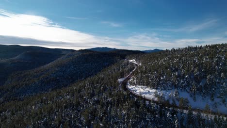 Drone-aerial-shot-of-a-bending-road-in-the-forest-with-mountains