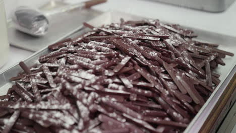 Sprinkle-Rack-Full-of-Dark-Brown-Chocolate-Sticks-with-Powdered-Sugar-in-Bakery,-Slow-Motion