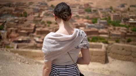 Chica-Caminando-Por-El-Pueblo-Marroquí-En-Un-Oasis-Del-Desierto-Con-Palmeras-Verdes-En-Un-Día-Caluroso-Y-Soleado,-Tiro-De-Mano