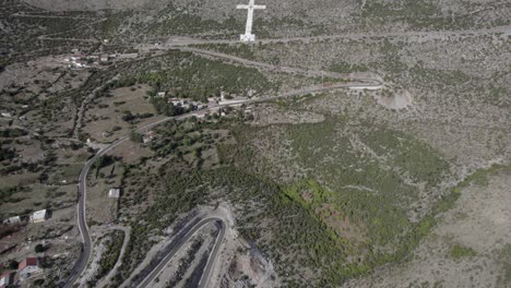 Video-De-Drones-De-Panorámica-Descriptiva-Sobre-El-Comienzo-Del-Paso-De-Montaña-De-La-Carretera-Sh20-En-Bridje,-Albania,-Vemos-La-Cruz-Blanca-Religiosa,-Se-Pueden-Ver-Las-Casas-Del-Pueblo,-Camino-Sinuoso