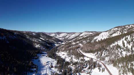 Aerial-drone-shot-over-a-snowy-valley-with-homes-and-a-bending-highway
