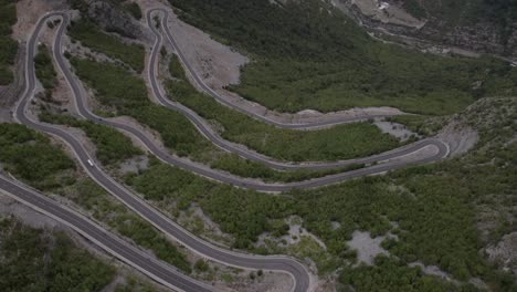 Drone-video-of-descriptive-panning-over-the-"Rrapsh-Serpentine"-mountain-pass-on-the-Sh20-road-in-Grabom,Albania,-you-can-see-a-motorcycle-and-car-passing-by