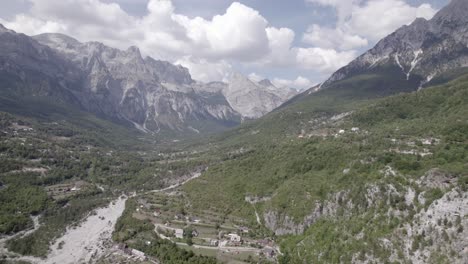 Frontal-drone-video-advancing-inside-the-theth-valley-in-albania,-over-the-river-Lumi-i-thethit-with-hardly-any-water,-with-Mount-Korab-in-the-background