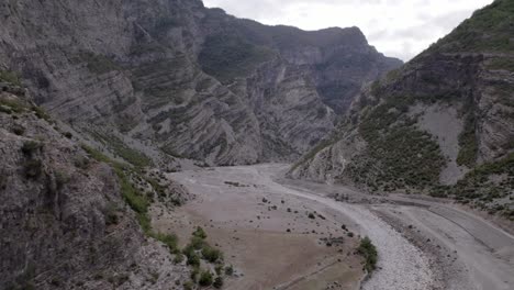 Drone-video-of-a-diagonal-plane-discovering-the-Sh20-highway-between-the-mountains-and-the-Cemi-river-in-Albania-at-the-height-of-Selce,-cloudy-sky-and-winding-road