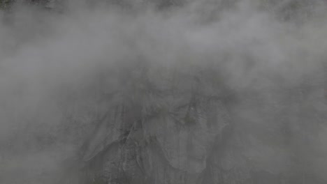 Heavy-fog-with-rocky-mountain-side-in-background,-aerial-side-flying-shot