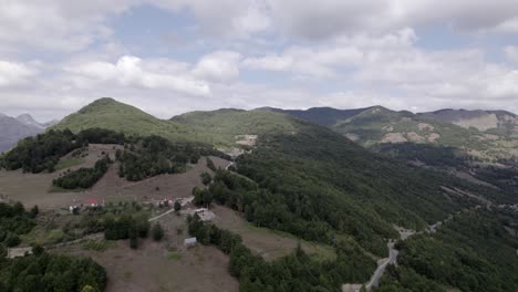 Video-with-descriptive-panning-Drone-advancing-on-the-Sh20-road-in-the-Lepushë-valley-in-Albania,-small-houses-of-the-town-can-be-seen,-somewhat-cloudy-sky