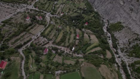 Video-Con-Drone-Panorámico-Descriptivo-Avanzando-En-La-Autopista-Sh20-En-Albania,-A-La-Altura-De-Javor-Y-Mreg,-Cielo-Nublado,-Casas-En-El-Pueblo-Y-Tierras-De-Cultivo