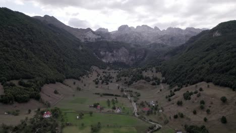 Drone-video-of-the-frontal-plane-advancing-over-the-Lepushë-valley-above-the-Lëpusha-river,-the-sh20-in-Albania,-you-can-see-small-houses-of-the-town,-a-somewhat-cloudy-sky-and-the-dry-river