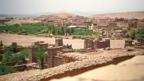 Moroccan-Village-in-a-Desert-Oasis-with-Green-Palm-Trees-on-a-hot-sunny-day,-rising-handheld-shot