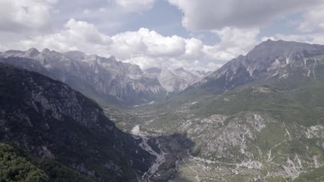 Frontal-drone-video-advancing-inside-the-theth-valley-in-albania,-over-the-river-Lumi-i-thethit-with-hardly-any-water,-with-Mount-Korab-in-the-background