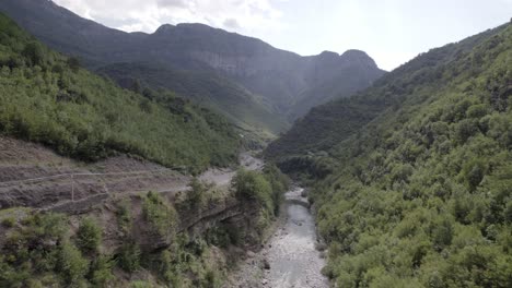 Drone-video-of-ascending-frontal-plane-advancing-over-the-interior-of-the-Cemi-river-on-the-Sh20-road-between-the-mountains-in-Albania-between-Tamarë-and-Selcë,-cloudy-sky-and-turquoise-river-waters