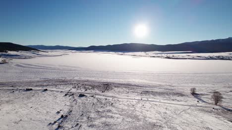 Aerial-drone-shot-of-a-frozen-lake-in-the-winter-on-a-sunny-day