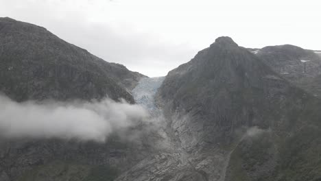 Icy-glacier-in-between-two-mountain-peeks-with-fluffy-clouds,-high-altitude-drone-shot