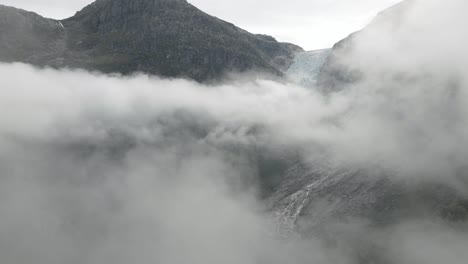 Rocky-mountain-standing-over-cloudscape-with-majestic-glacier,-aerial-drone-shot
