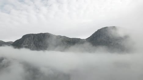 Picos-De-Montaña-Rocosa-De-Pie-Sobre-Nubes-Esponjosas,-Vista-Aérea