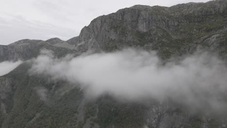 Massive-rocky-mountain-standing-above-cloudscape,-high-altitude-drone-shot