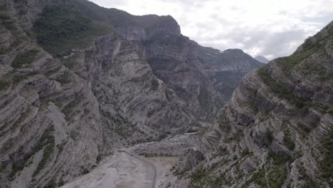 Drone-video-of-frontal-plane-advancing-discovery-on-the-Sh20-road-between-the-mountains-and-the-cemi-river-in-Albania-at-the-height-of-Selce,-cloudy-sky-and-winding-road