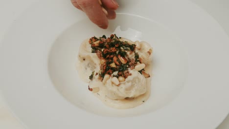 Plating-dumplings-in-yogurt-cream-dish,-adding-pine-tree-seeds