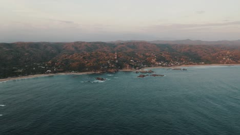 Drone-Panorama-shot-of-beautiful-coastline-of-Mazunte-with-massive-mountains-in-background-during-misty-day---Mexico,Punta-Cometa