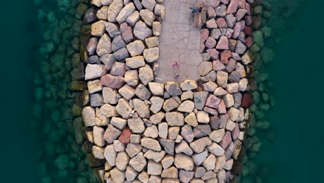 Aerial-view-of-people-on-a-walkable-breakwater-made-out-of-rocks-in-very-clear-water