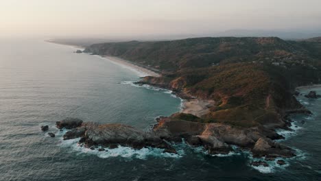 Luftaufnahme-Des-Wunderschönen-Punta-Cometa-Aussichtspunkts-Und-Des-Mazunte-Strandes-Mit-Küstenlinie-Im-Hintergrund-Während-Des-Nebligen-Sonnenuntergangs-In-Mexiko