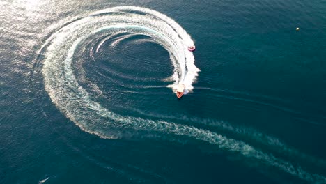 Top-down-view-of-speed-boat-towing-a-big-ski-or-wakeboard-turning-in-a-circle-against-a-deep-blue-water-background