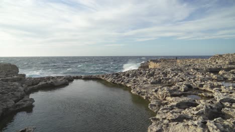 Steinplateau-In-Der-Nähe-Des-Azurblauen-Fensters-Auf-Der-Insel-Gozo-Mit-Massiven-Wellen,-Die-An-Der-Küste-Zusammenbrechen