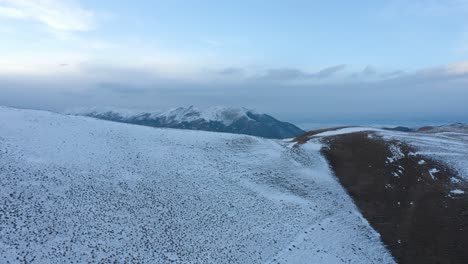 Drohne,-Die-über-Einen-Schneebedeckten-Hang-Aufsteigt-Und-Majestätische-Berge-Im-Hintergrund-Enthüllt