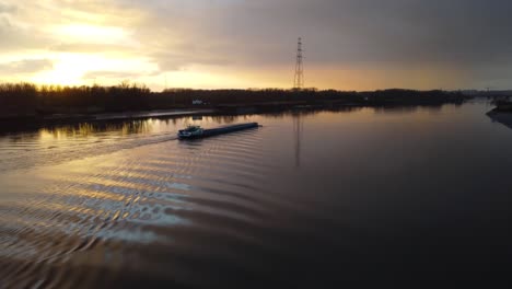 Cargo-barge-boat-sailing-in-river-Scheldt-during-golden-sunset,-aerial-ascend-shot