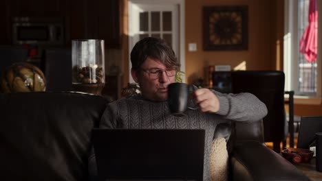älterer-Mann-Trinkt-Kaffee,-Während-Er-Auf-Einer-Couch-Sitzt-Und-Zu-Hause-Arbeitet