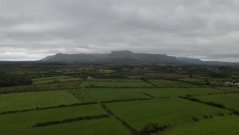 Drone-shot-of-green-fields-with-a-mountain-range-in-the-background